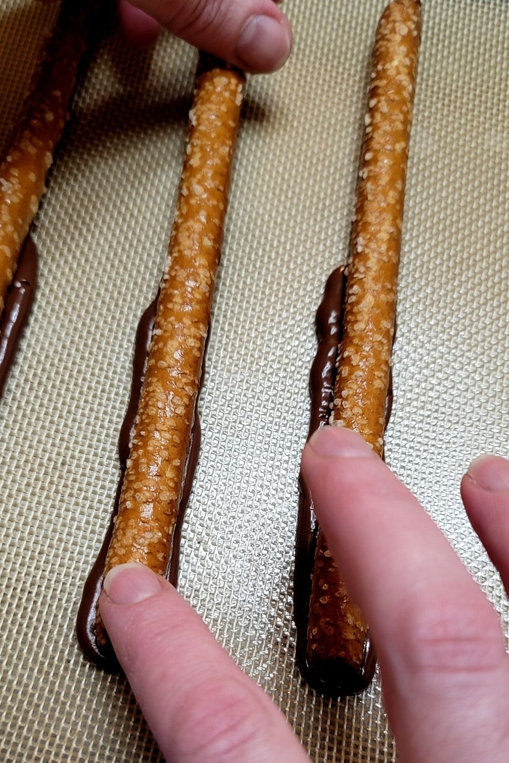 press pretzel into piped chocolate on silicone sheet for caramel chocolate pretzel logs