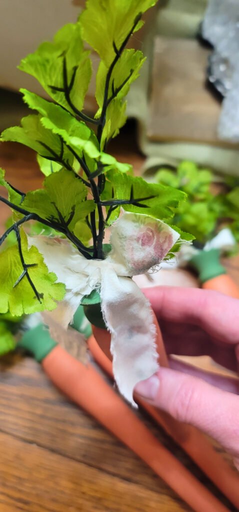 A close-up image of an artificial carrot with green leaves and a white fabric bow, reminiscent of a Reclaimed Chair Spoindle project.